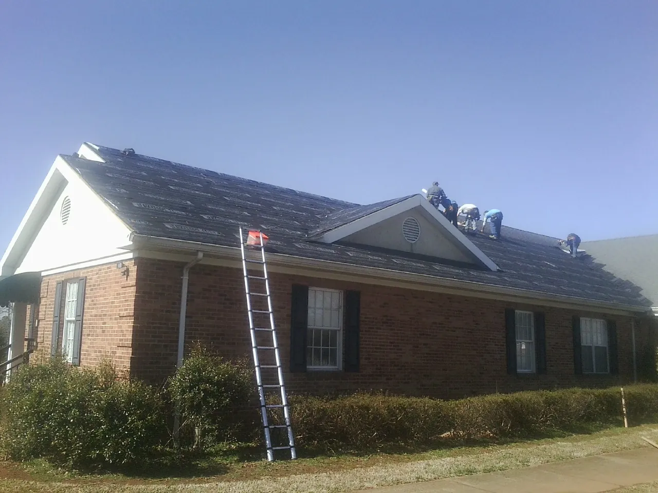 Crew tearing shingles off a brick ranch roof with a ladder set — Emergency Roof Repair work by our crew in Yucaipa