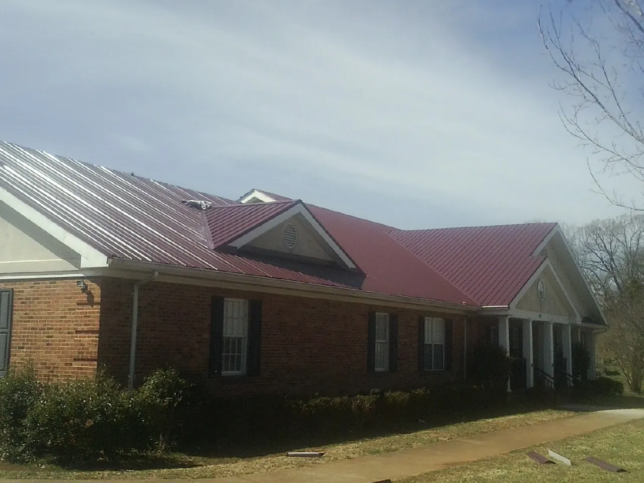 Red metal roof with gabled entries on a long brick building, from a Hail Damage Roof Repair job in Yucaipa