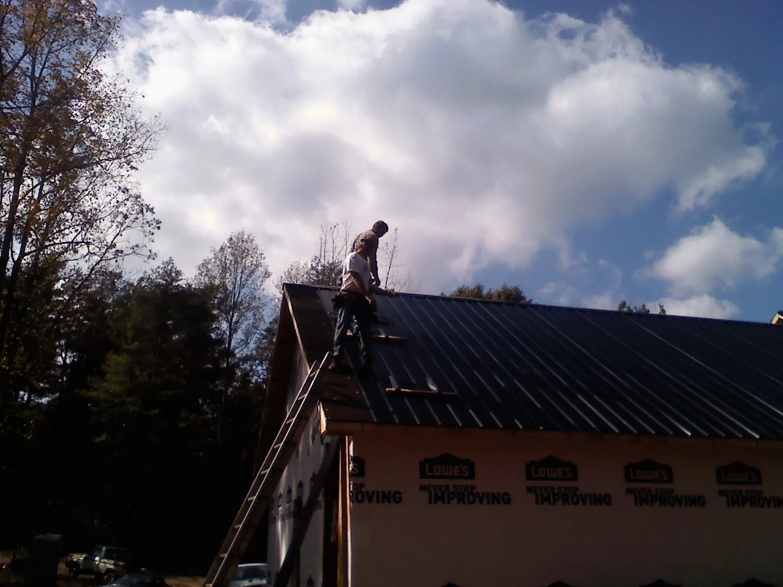 Roofer fastening dark metal panels high against a cloudy sky, from a Roof Inspection job in Yucaipa
